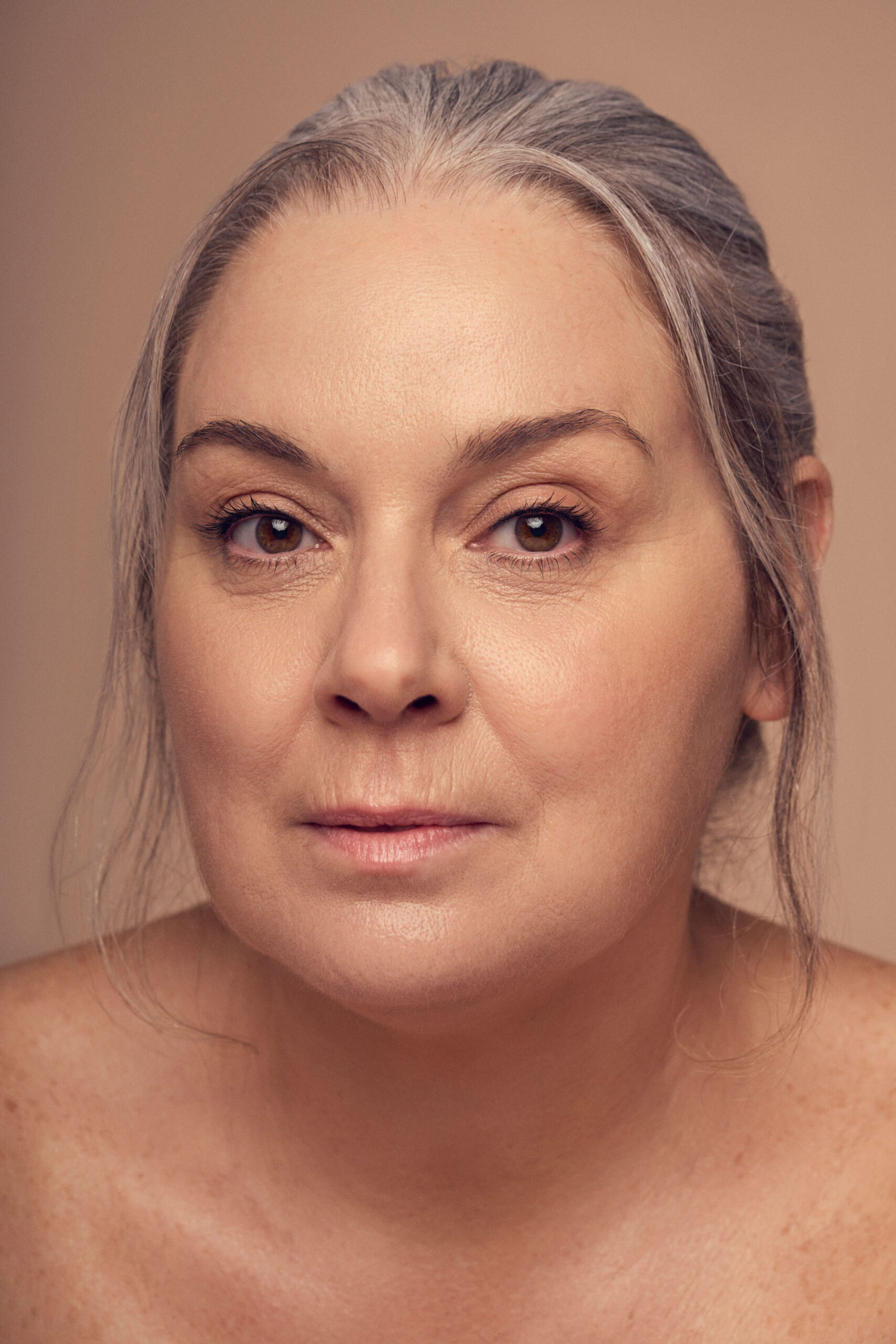 A woman with gray hair pulled back gazes into the camera against a neutral background. Her expression is calm and serene.