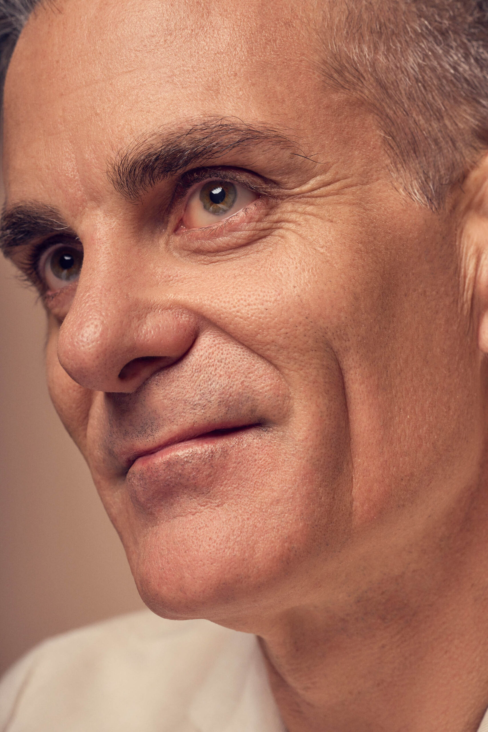 Close-up of a middle-aged man with short, graying hair and a gentle smile. He has a contemplative expression, with visible fine lines around his eyes. The lighting is warm and soft, highlighting the texture of his skin.