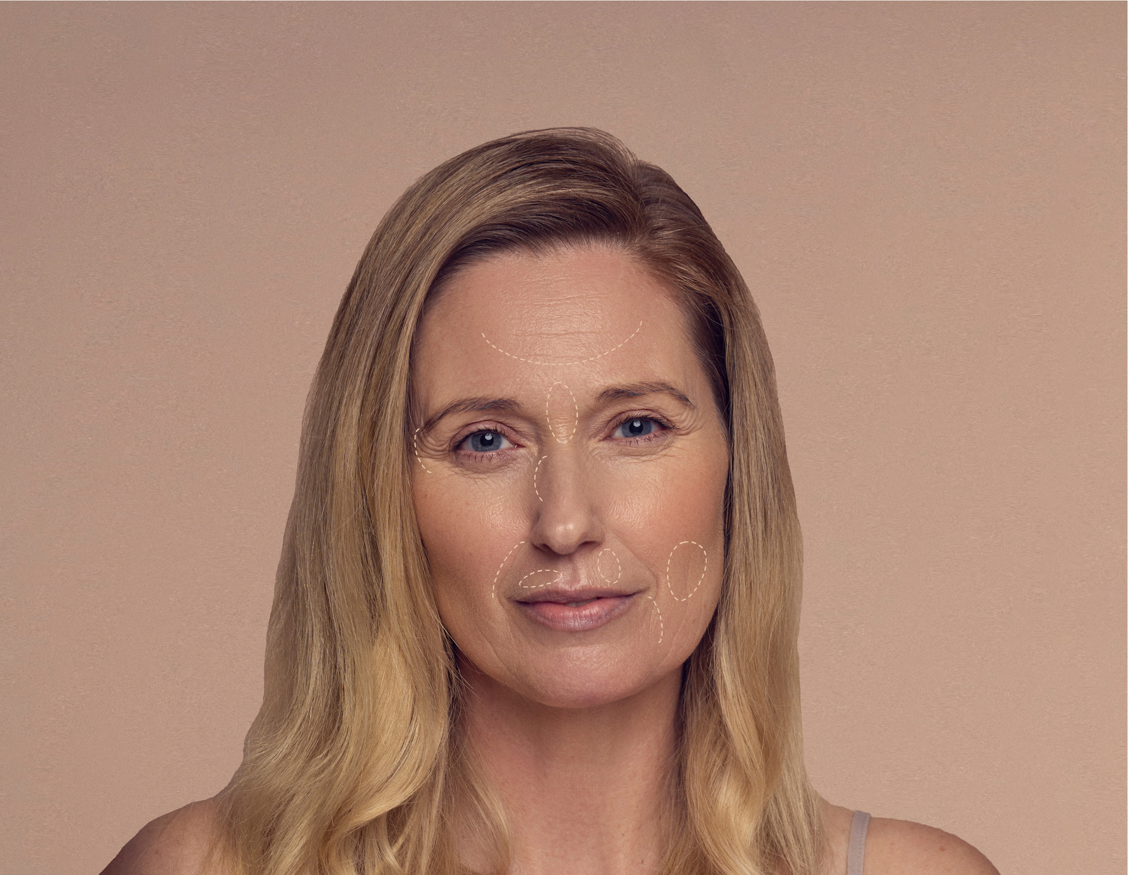 Woman with long blonde hair smiles softly against a peach background. Her face is decorated with delicate white line drawings highlighting her facial features. Shes wearing a simple top.