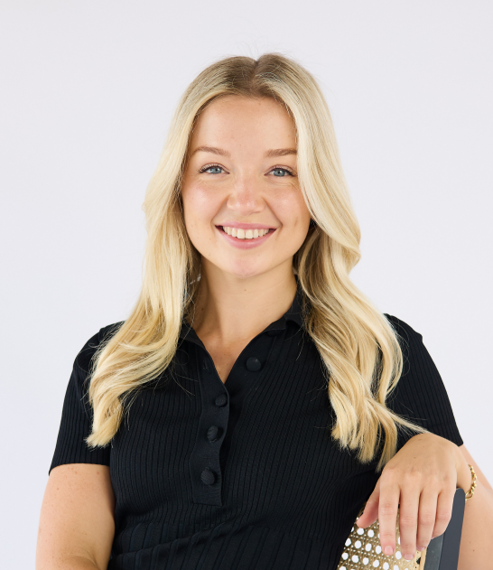 A smiling young woman with blonde hair wearing a black polo shirt.